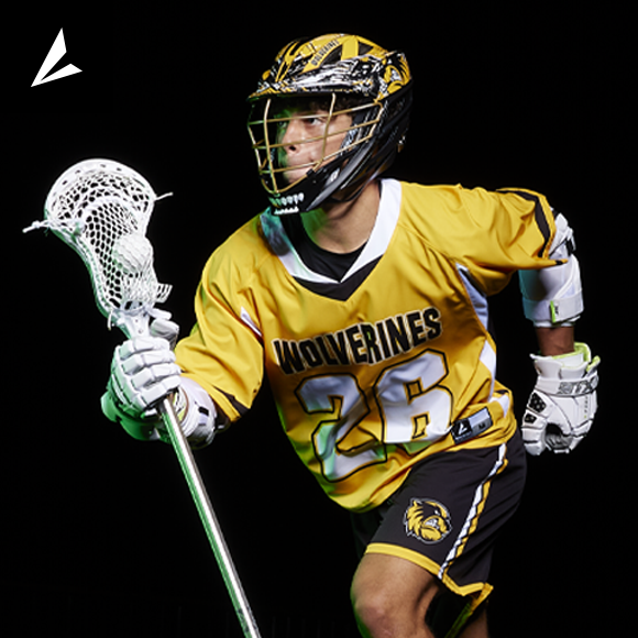  lacrosse player wearing a BSN Victory Sports uniform running and equipped with a helmet and gloves, holding a lacrosse stick. With a ball in the netting. 