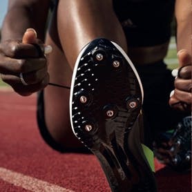 A track athlete tying their adidas track spikes
